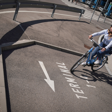 Frau fährt mit dem Fahrrad auf ausgeschildertem Weg Richtung Terminal am Flughafen Stuttgart