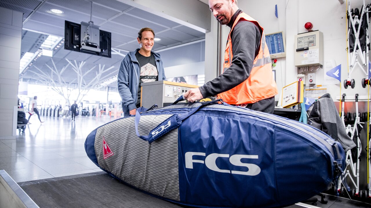 Flughafenmitarbeiter nimmt am Schalter für Sperrgepäck ein Surfbrett in Schutzhülle entgegen