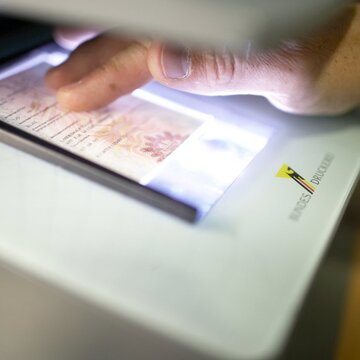 Hand legt einen Ausweis zur Echtheitsprüfung auf ein Lichtprüfgerät