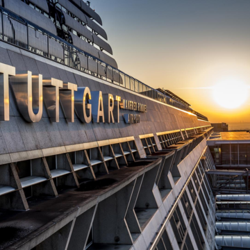 Sonnenaufgang am Flughafen Stuttgart: Blick entlang der Terminalfassade mit großem Schriftzug „STUTTGART MANFRED ROMMEL AIRPORT“.