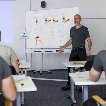 Ein Ausbilder erklärt an einem Whiteboard Inhalte vor mehreren Teilnehmenden in einem Schulungsraum am Flughafen Stuttgart.