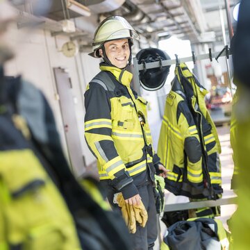  Feuerwehrmann in gelber Schutzkleidung lacht und steht in einer Umkleide der Flughafenfeuerwehr Stuttgart.