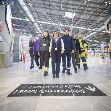 Team aus verschiedenen Berufsgruppen läuft gemeinsam durch die lichtdurchflutete Abflughalle des Flughafens Stuttgart.