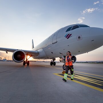 Eine Bodenmitarbeiterin läuft vor einem Flugzeug über das Vorfeld des Flughafens Stuttgart bei Sonnenuntergang.