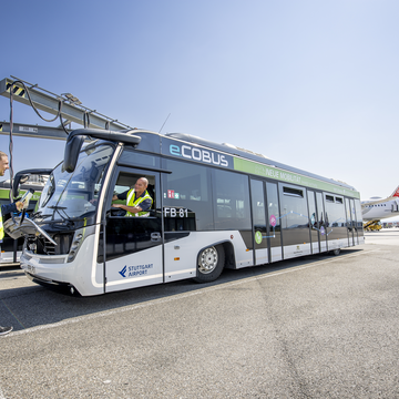 Ein Busfahrer spricht mit einem anderen Mitarbeiter auf dem Vorfeld, der seinen Elektro-Passagierbus zum Laden einsteckt.