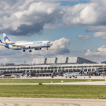 Flugzeug im Landeanflug vor dem Terminalgebäude des Flughafens Stuttgart bei blauem Himmel mit Wolken.