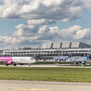 Mehrere Flugzeuge verschiedener Airlines rollen vor dem Terminal des Flughafens Stuttgart bei leicht bewölktem Himmel.