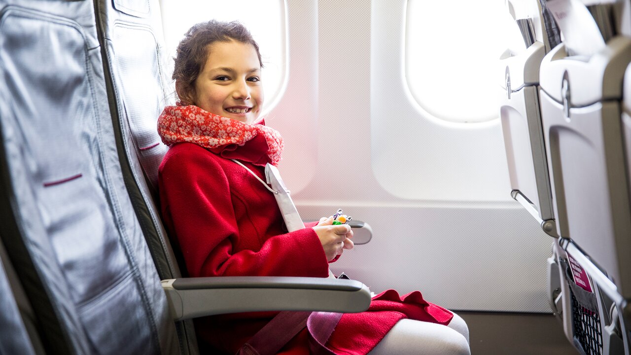 Person in roter Kleidung sitzt im Flugzeug und hält ein Spielzeug. 