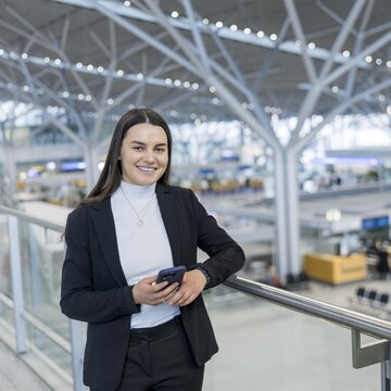Person steht mit einem Smartphone auf einer Galerie im Flughafen Stuttgart, mit Blick auf den Terminalbereich.