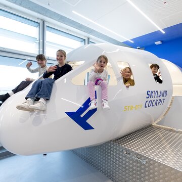 Kinder sitzen in einer Flugzeugnachbildung im Skyland Cockpit Bereich des Flughafen Stuttgart.