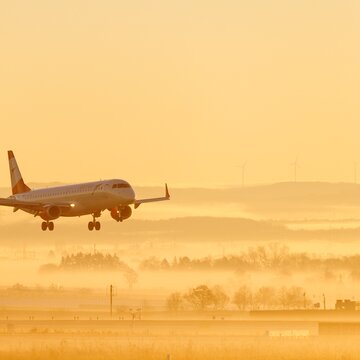 Ein Flugzeug landet bei Sonnenaufgang auf dem Flughafen Stuttgart, umgeben von Nebel und sanften Farben.
